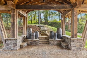 A covered outdoor area with stone steps leading up to a wooden structure, surrounded by trees.