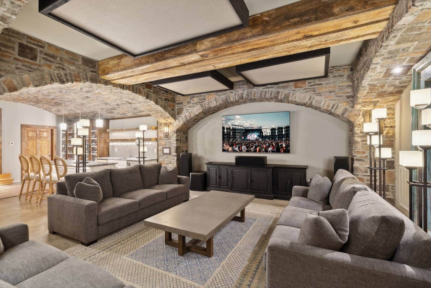 A spacious living area with a stone wall, a large flat-screen TV mounted on the wall, and a seating arrangement including sofas and a coffee table.
