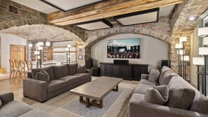 A spacious living area with a stone wall, a large flat-screen TV mounted on the wall, and a seating arrangement including sofas and a coffee table.