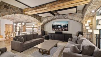 A spacious living area with a stone wall, a large flat-screen TV mounted on the wall, and a seating arrangement including sofas and a coffee table.