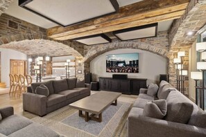 A spacious living area with a stone wall, a large flat-screen TV mounted on the wall, and a seating arrangement including sofas and a coffee table.
