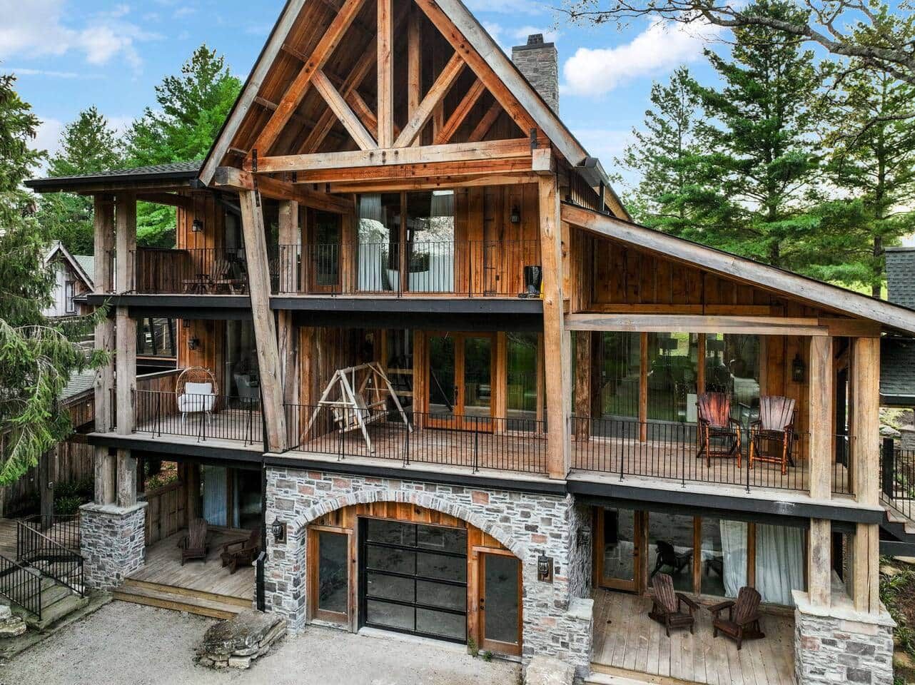 Une cabane en rondins à plusieurs étages, dotée de fondations en pierre, de grandes fenêtres et d’espaces de détente extérieurs.
