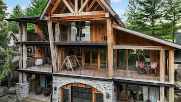 Une cabane en rondins à plusieurs étages, dotée de fondations en pierre, de grandes fenêtres et d’espaces de détente extérieurs.