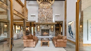 A spacious living room with a stone fireplace, leather sofas, and a chandelier.