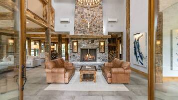 A spacious living room with a stone fireplace, leather sofas, and a chandelier.