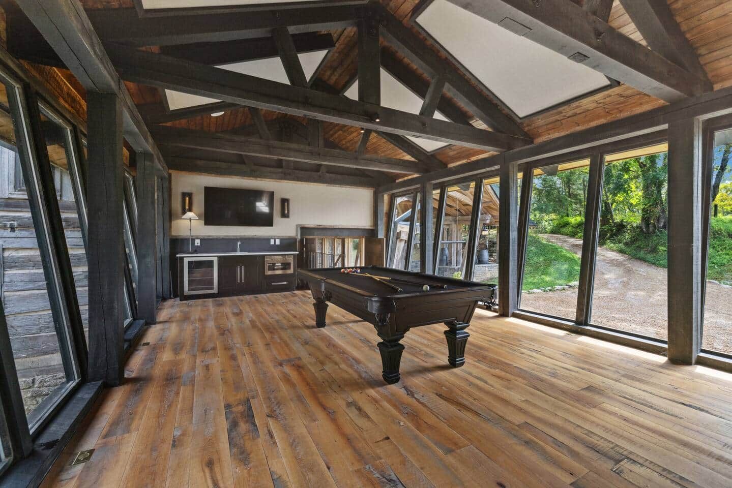 A pool table in a room with wooden flooring and large windows.
