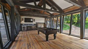 A pool table in a room with wooden flooring and large windows.