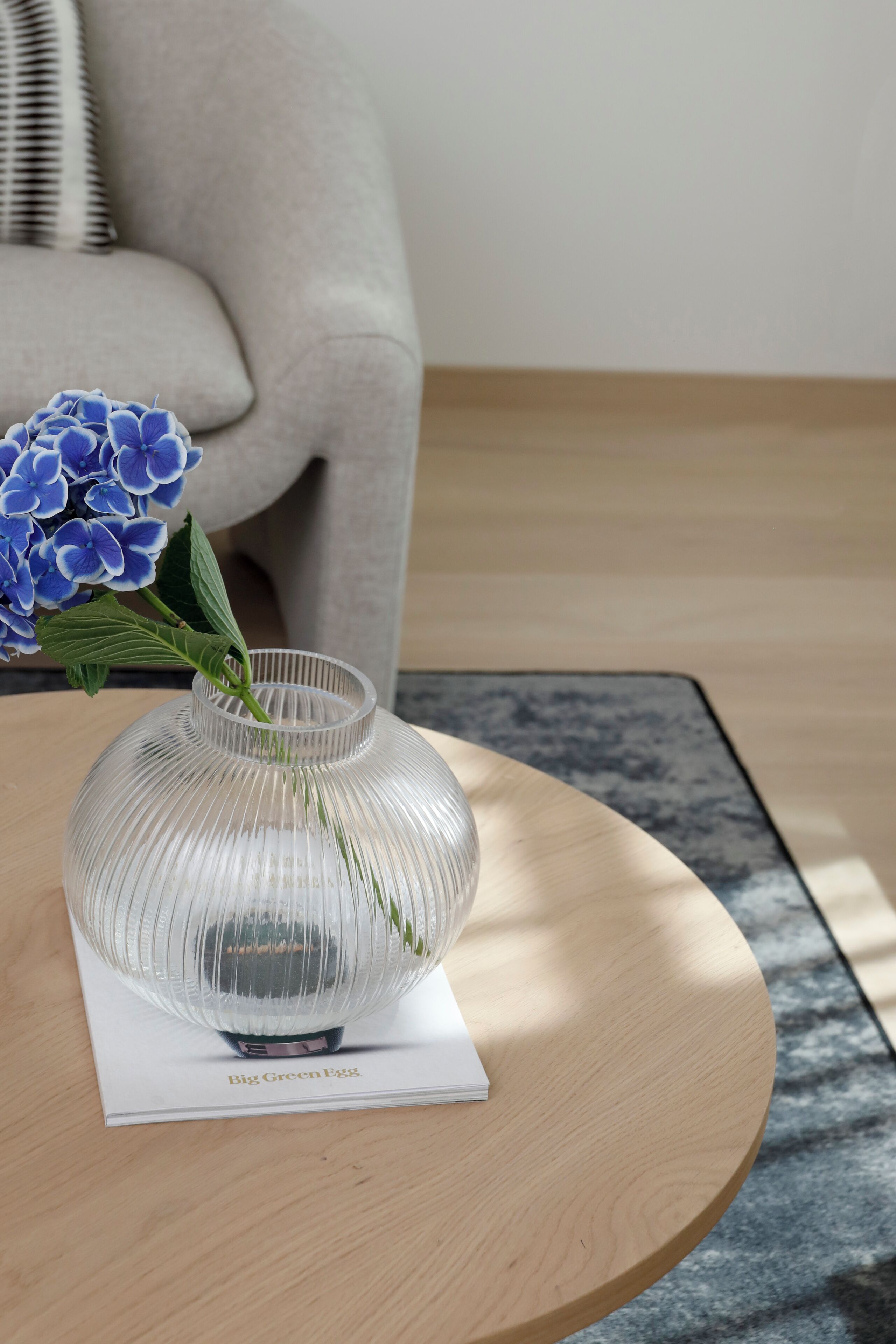 Un vase en verre transparent, doté d’un pied et d’une étiquette, est posé sur une table ronde en bois.