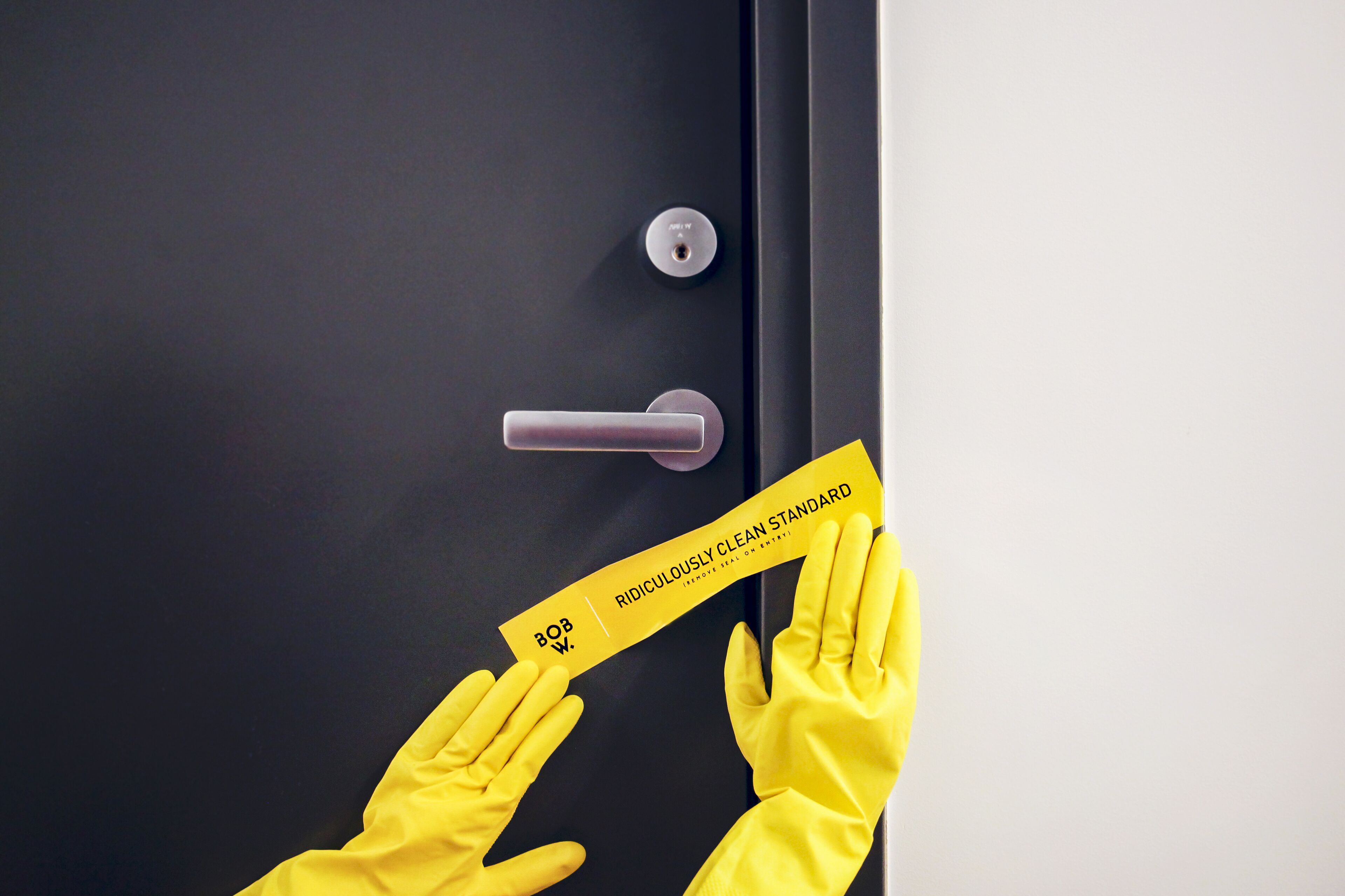 A person wearing yellow gloves holding a yellow card with text near a door.
