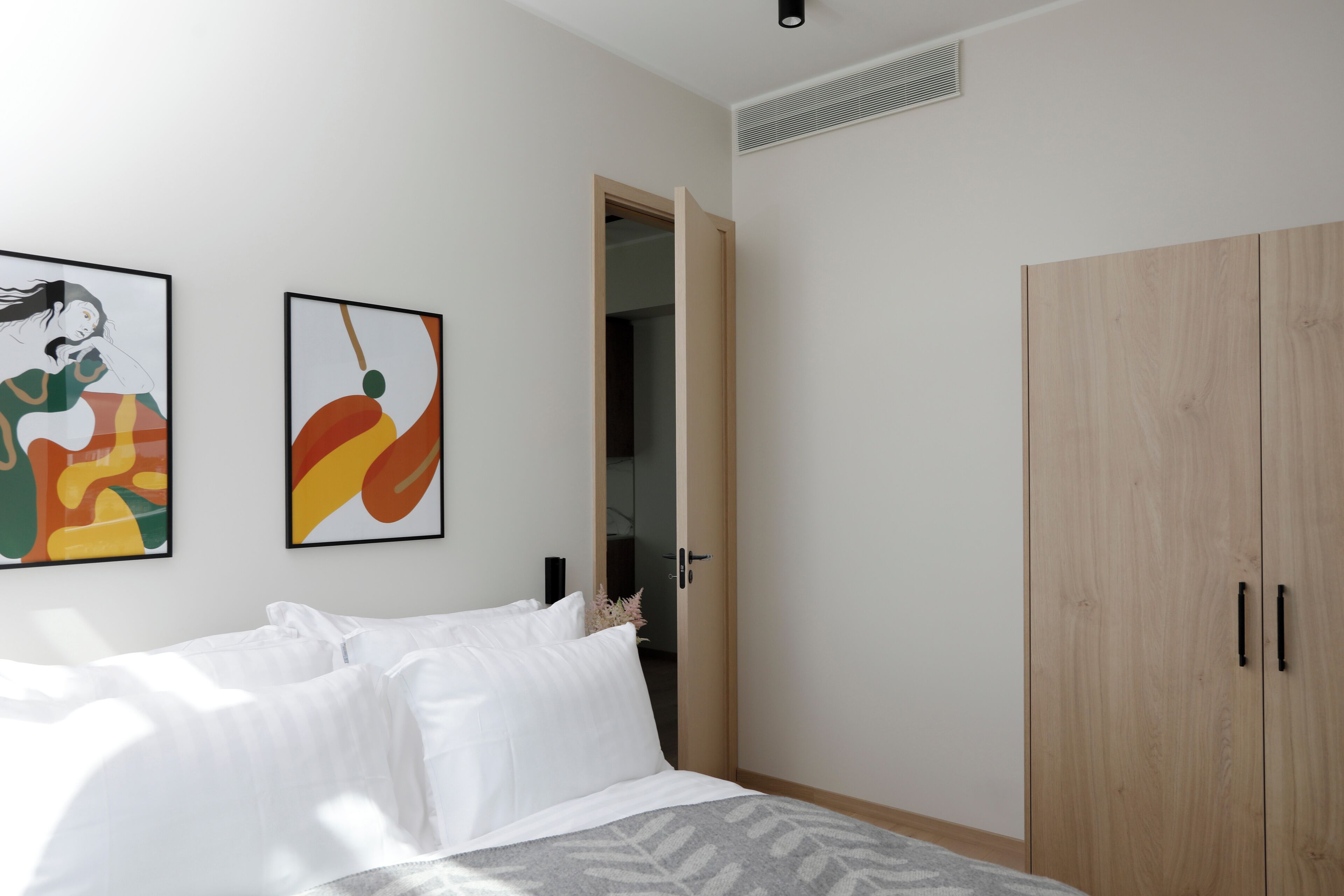 Een slaapkamer met een bed, een kledingkast en twee abstracte schilderijen aan de muur.