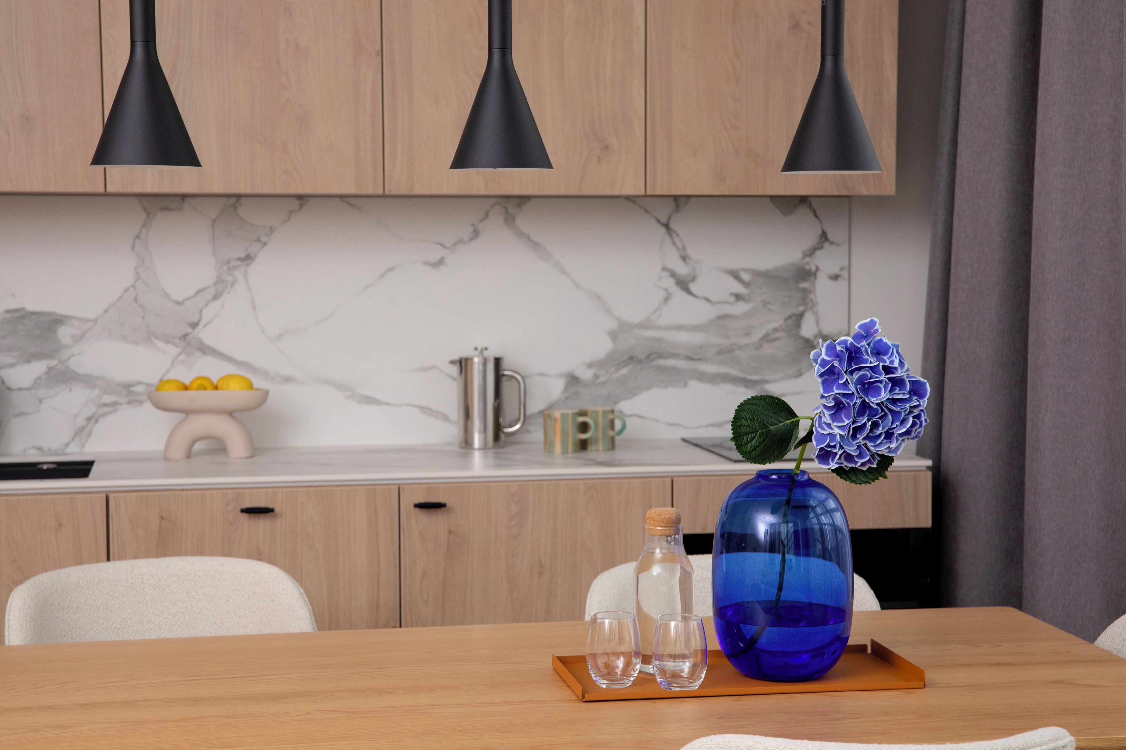 A modern kitchen with wooden cabinets, marble backsplash, and pendant lighting.