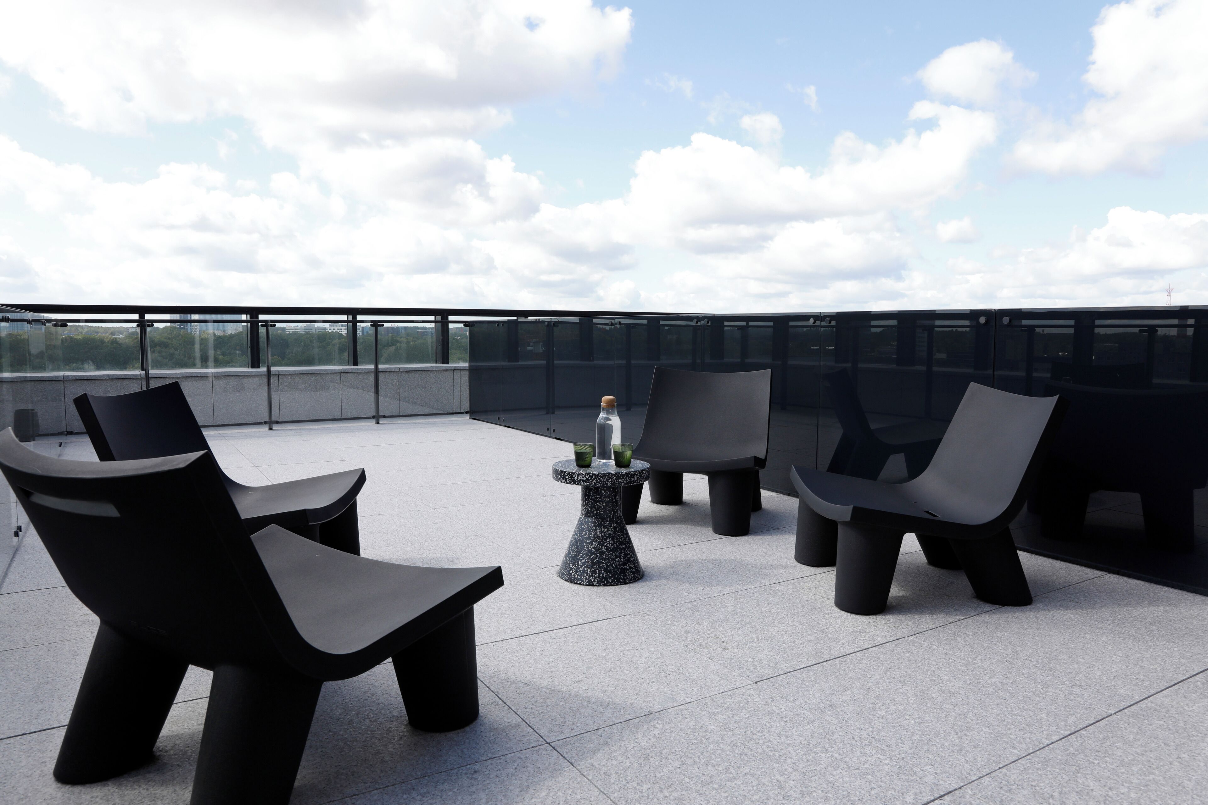 Terraço no telhado com mobiliário preto moderno, incluindo cadeiras e uma mesa, e vista desobstruída do céu.