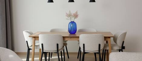 A dining area with a wooden table, six chairs, a blue vase with flowers, and three pendant lights.