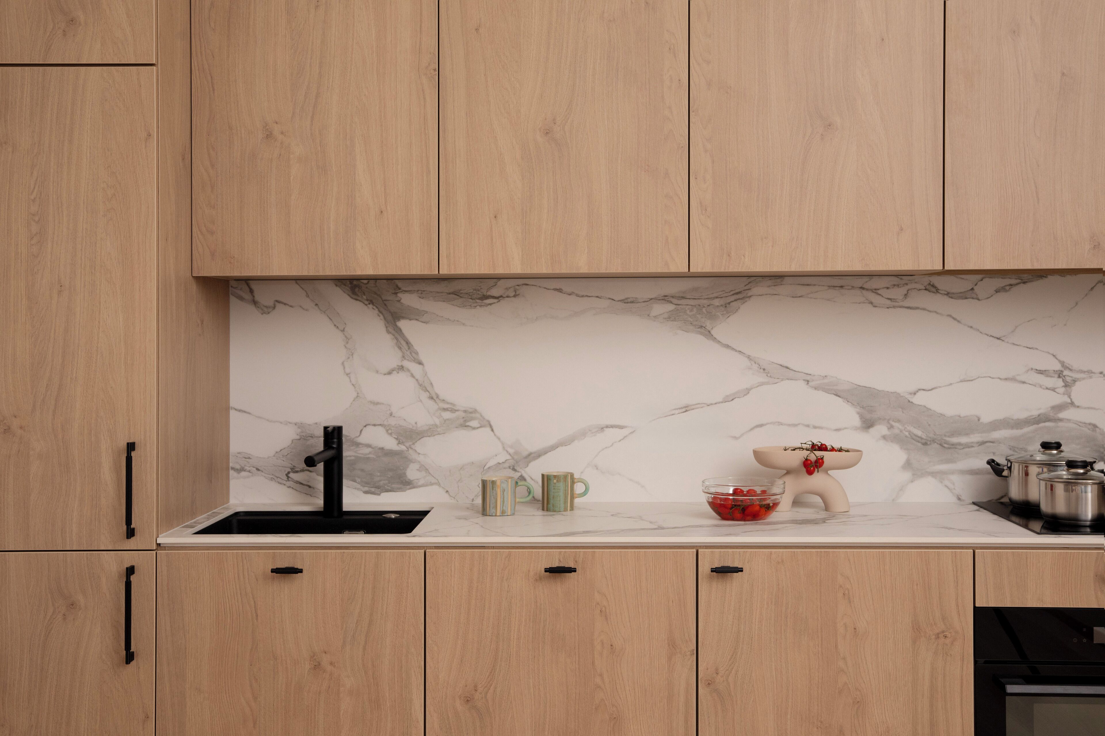 Uma cozinha com armários de madeira, painel de fundo de mármore, pia e diversos utensílios de cozinha.