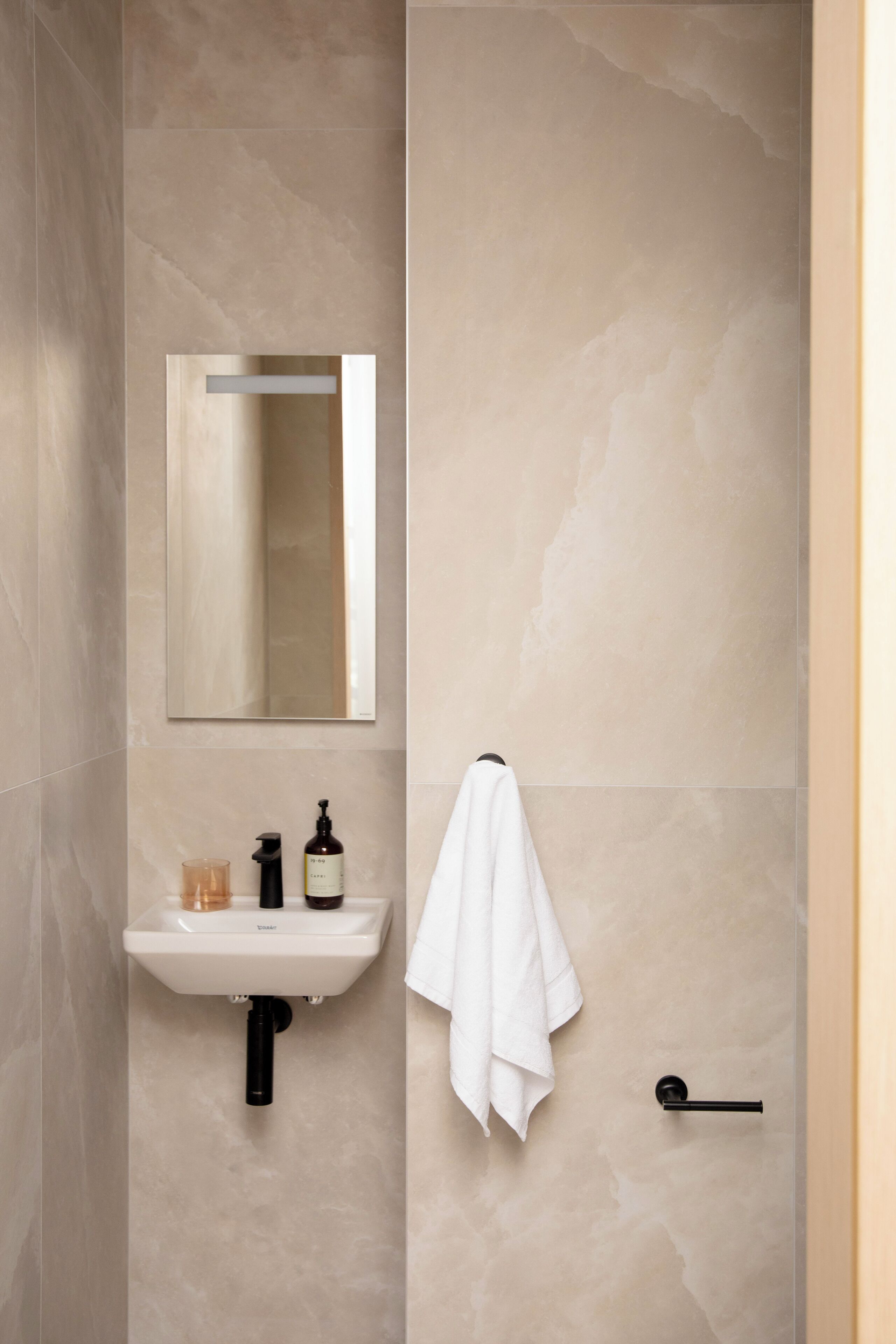 A bathroom with a white sink, a mirror, a towel hanging on a rack, and a door with a handle.