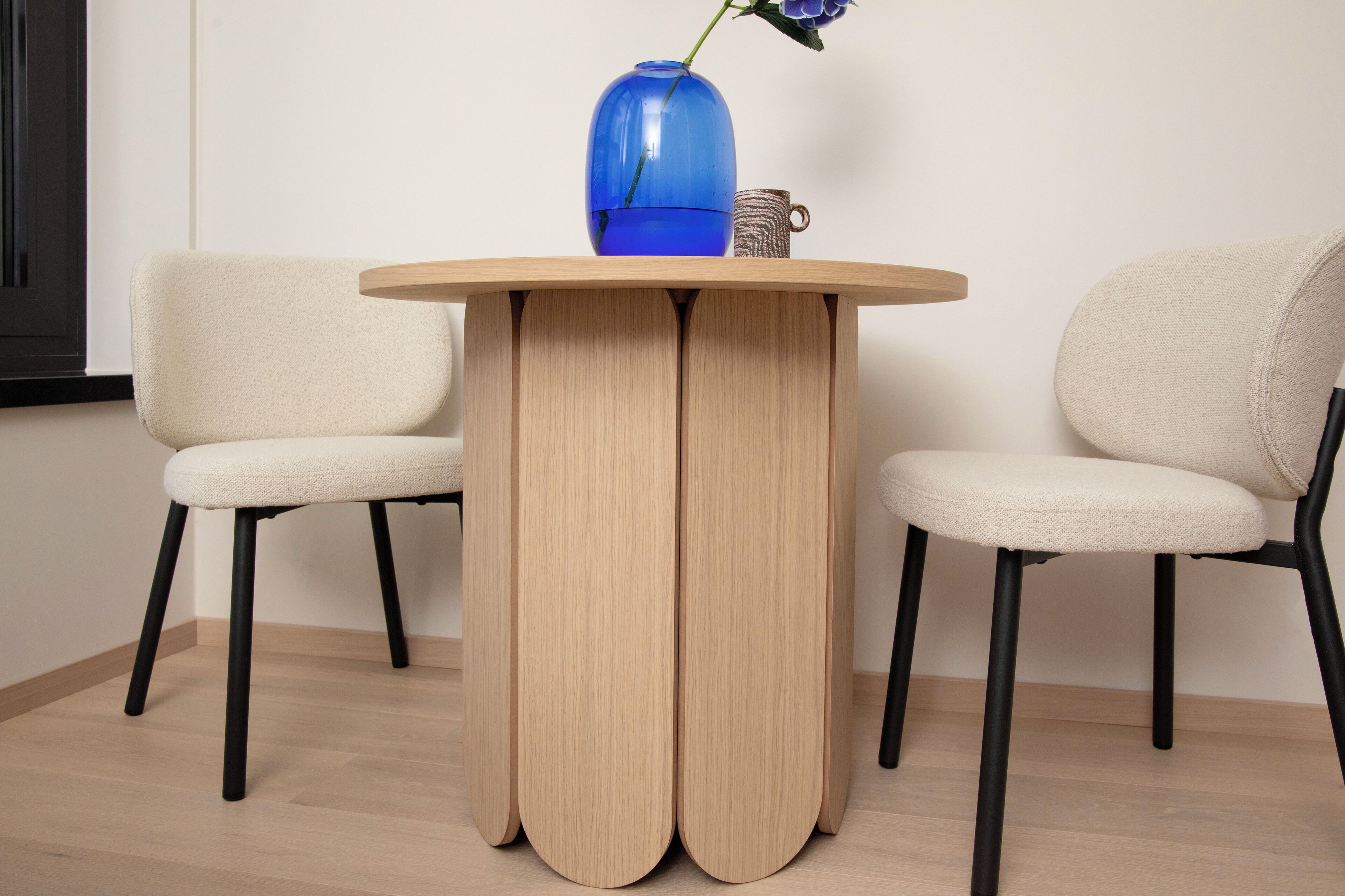 Une table ronde en bois, sur laquelle sont posés un vase et une tasse, et deux chaises de chaque côté.