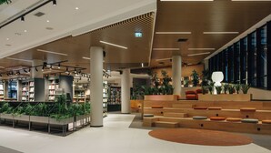 A modern library interior with bookshelves, seating areas, and a central staircase.