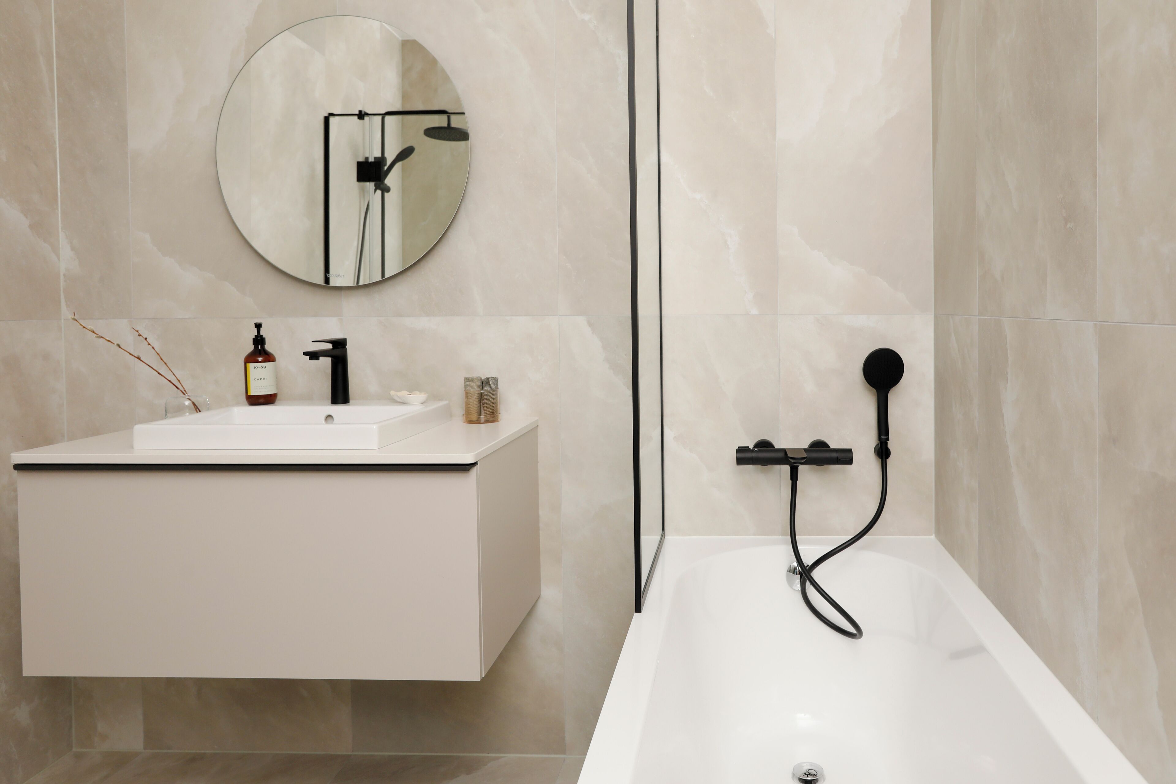 A modern bathroom with a white vanity, a round mirror, a bathtub, and a handheld showerhead.