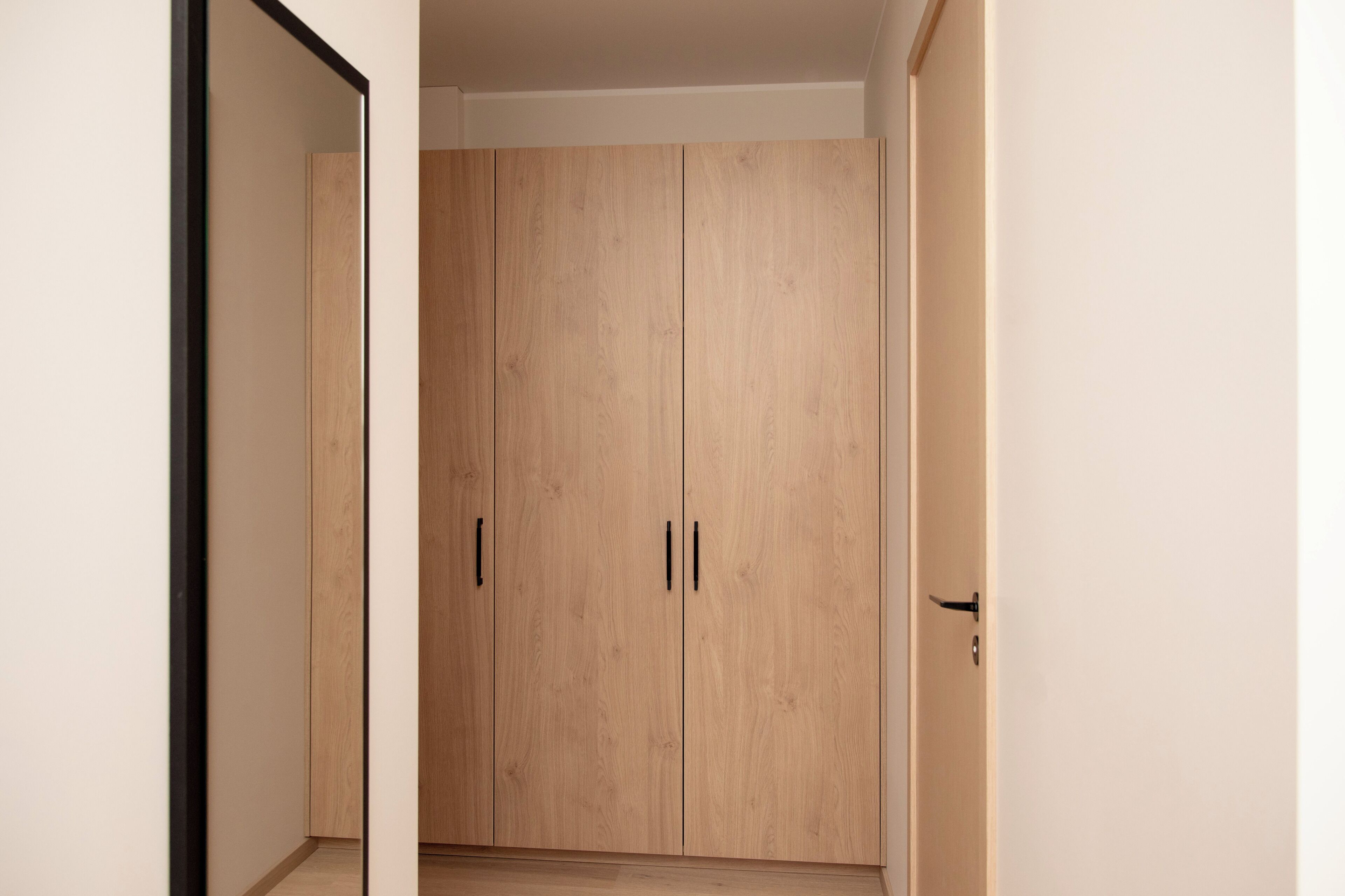 Ein Flur, der zu einem Holzschrank mit zwei Türen und schwarzen Griffen führt.
