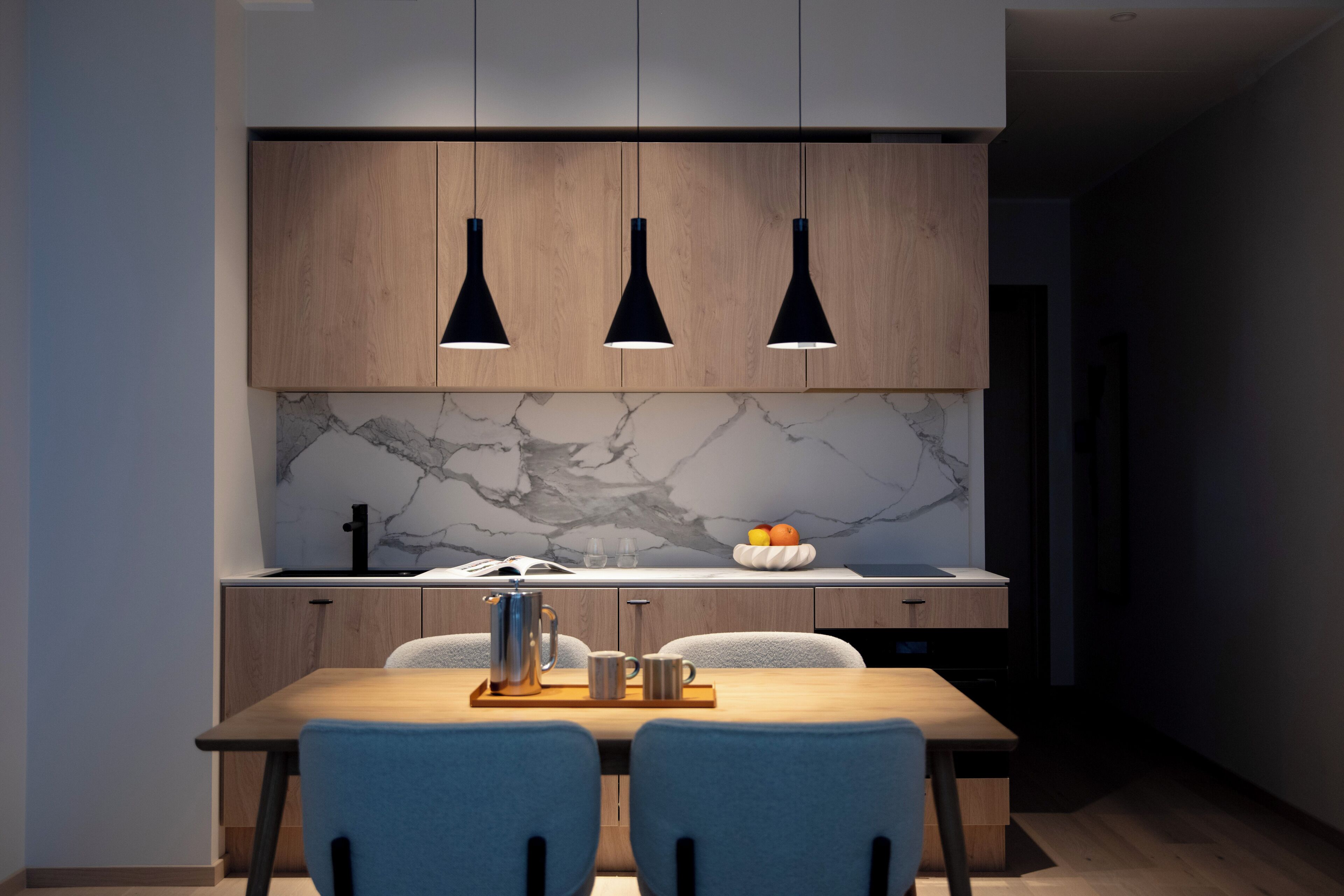 A modern kitchen with wooden cabinets, a marble backsplash, and a dining table with chairs.