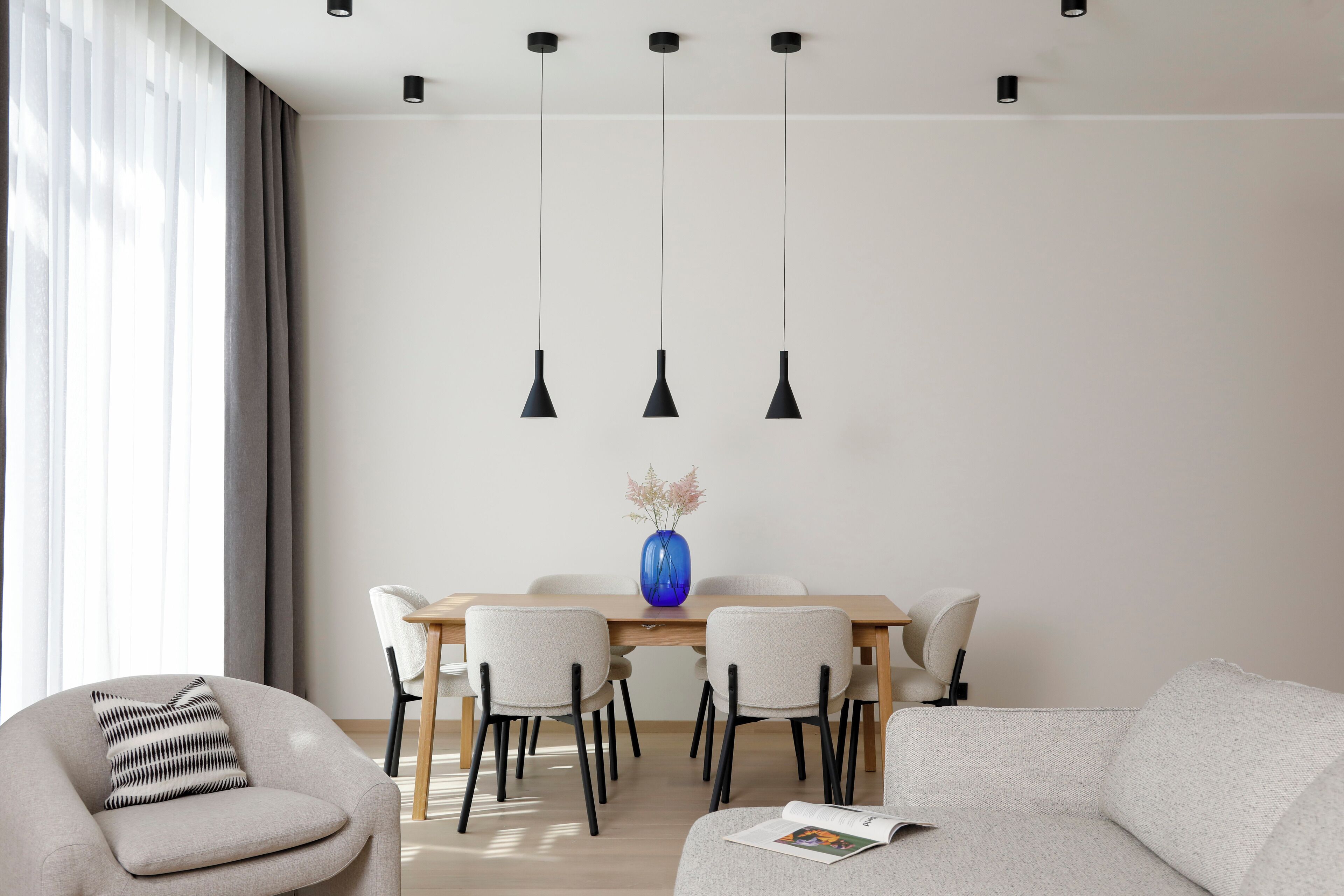 A modern dining area with a wooden table, six chairs, and three pendant lights.