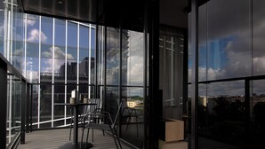 A modern balcony with a glass wall, a table with chairs, and a view of the cityscape.