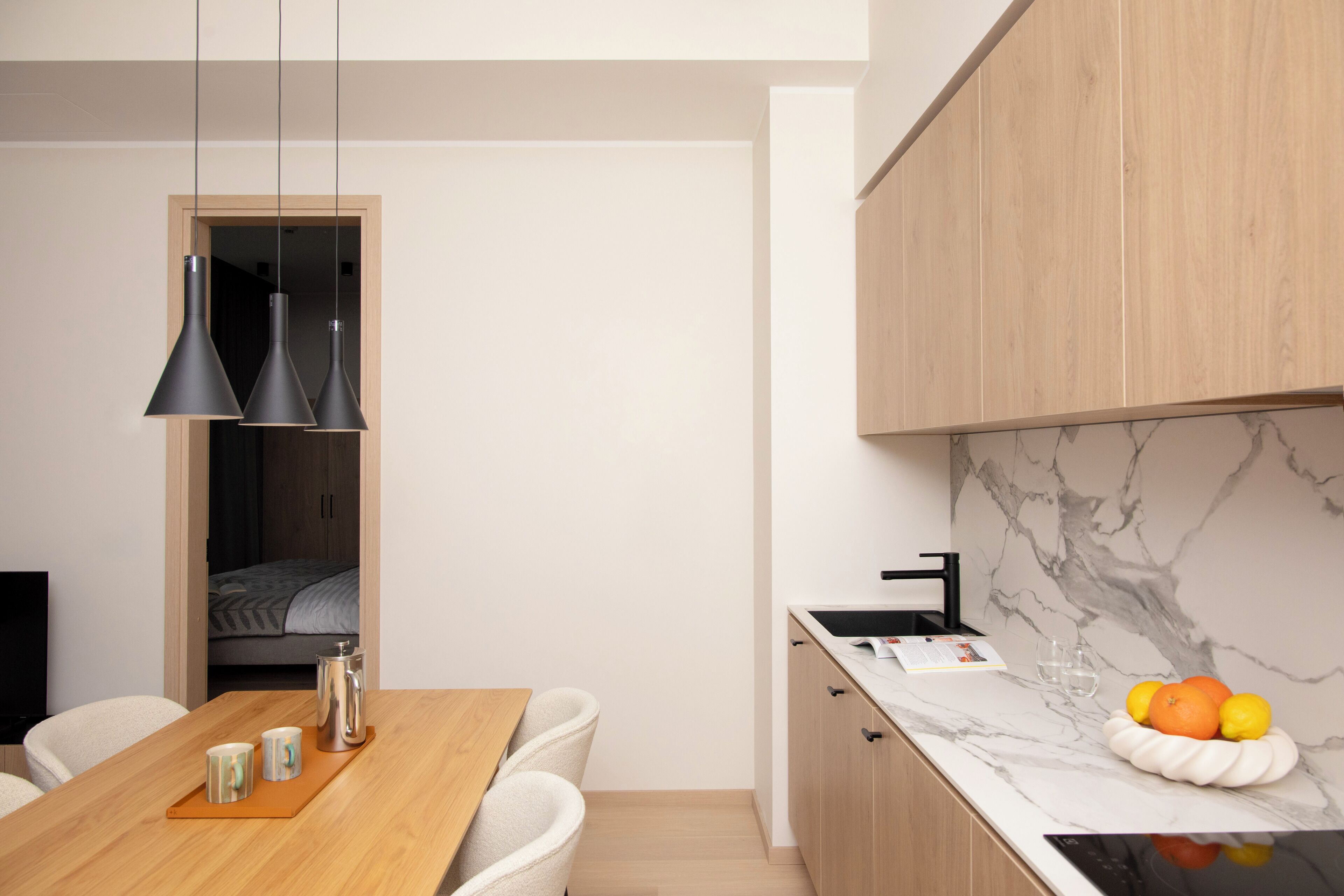 A modern kitchen with wooden cabinets, a marble backsplash, and a fruit bowl on the counter.
