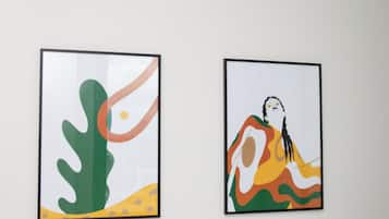 Two framed artworks on a plain wall above a white bed with white bedding.