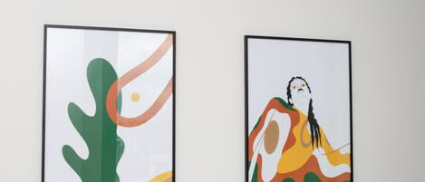 Two framed artworks on a plain wall above a white bed with white bedding.