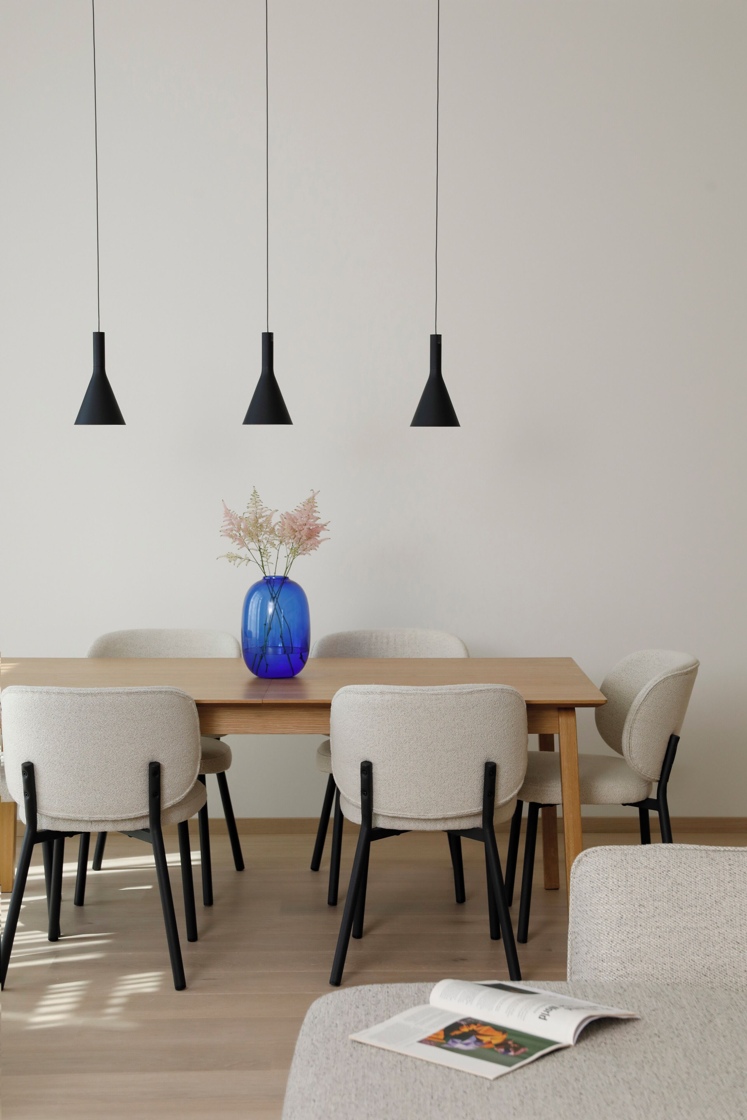 A dining area with a wooden table, six chairs, and three pendant lights.