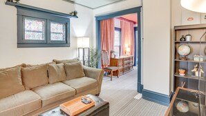 A living room with a beige sofa, a coffee table with a tray, a bookshelf with decorative items, and a view into another room through an open door. - Charming Minneapolis Home w/ Deck, 5 Mi to Central (Minneapolis)
