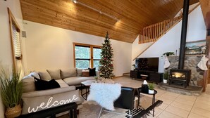 Ein gemütliches Wohnzimmer mit einem Ecksofa, einem Weihnachtsbaum, einem Kamin und einer Treppe.
