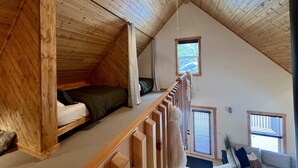 Ein Schlafzimmer im Loft-Stil mit schrägem Dach, einem Bett, einem Fenster und einem Deckenventilator.