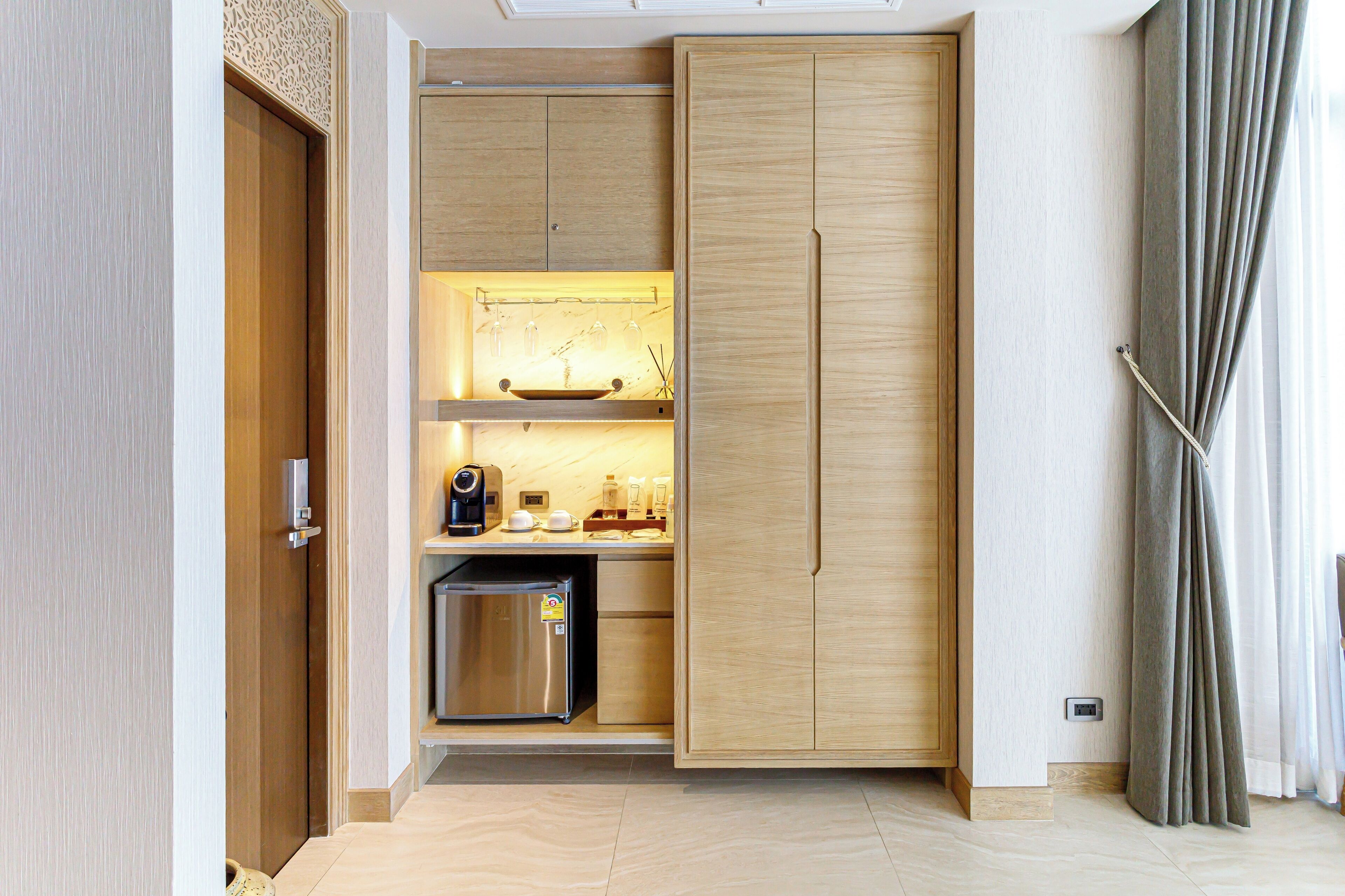 Una cocina compacta con un refrigerador integrado, una cafetera y una estantería con cristalería.