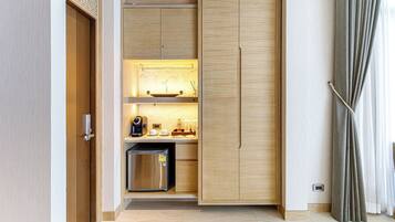 Una cocina compacta con un refrigerador integrado, una cafetera y una estantería con cristalería.