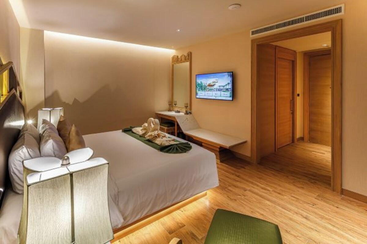 Quarto de hotel com cama, escrivaninha, cadeira, televisão e porta.