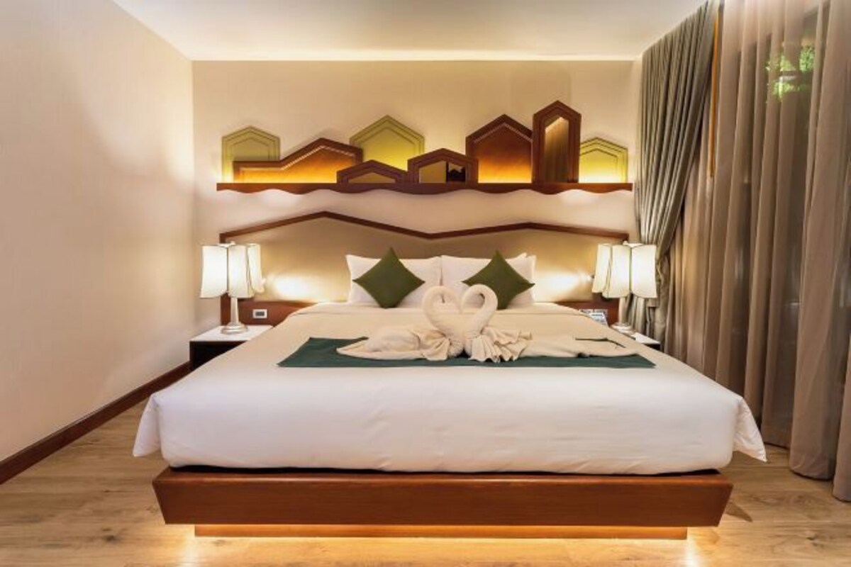 Quarto de hotel moderno com cama grande, cabeceira de madeira e iluminação ambiente.