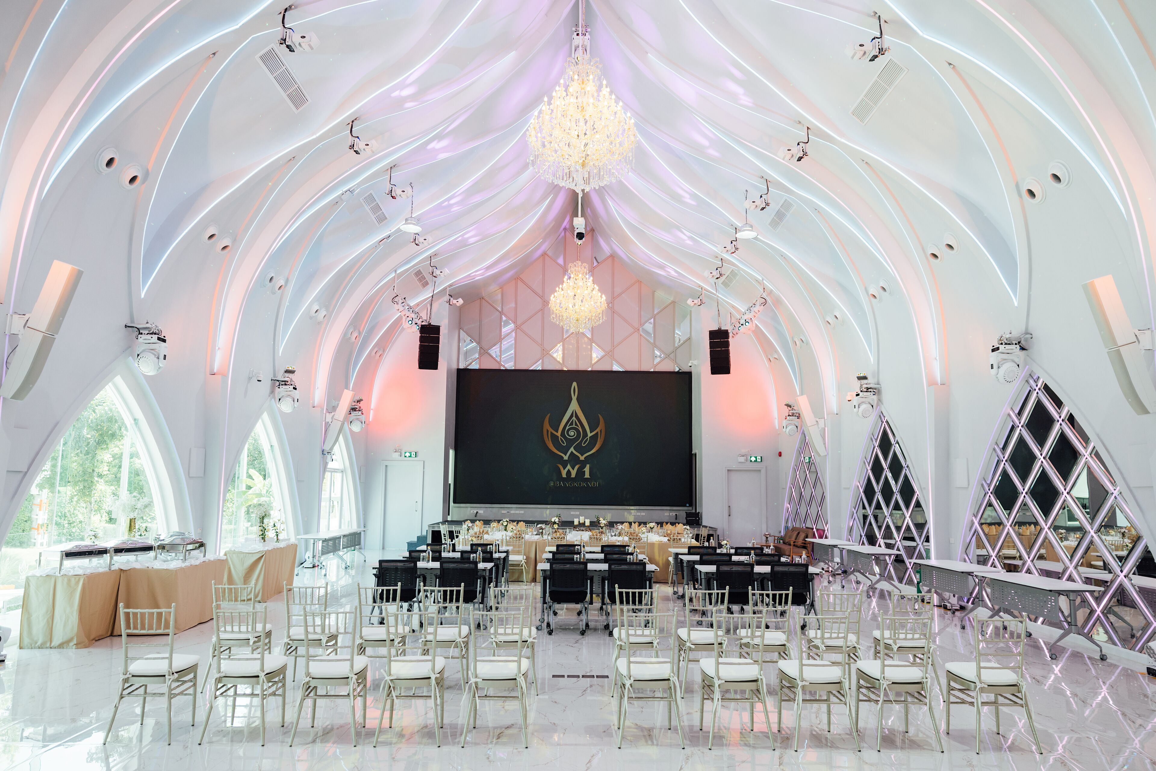 A spacious hall with a stage, rows of chairs, and a large screen displaying a logo.