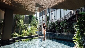A woman in a black swimsuit standing at the edge of a pool with a wooden ceiling and a staircase in the background.