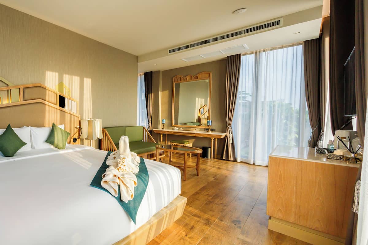 Une chambre d’hôtel avec un grand lit, un bureau, une chaise, un miroir et une commode.