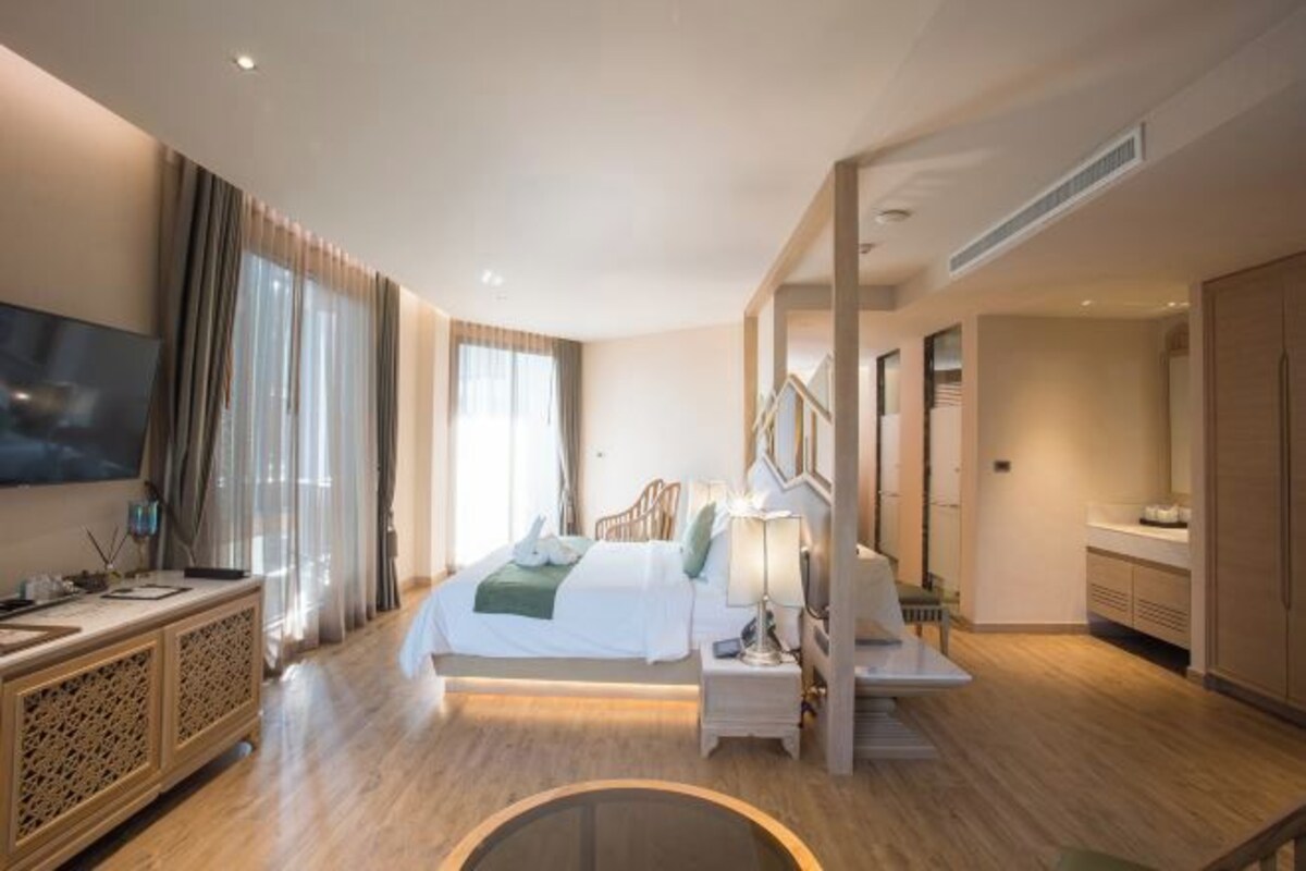 Quarto de hotel moderno com uma cama grande, televisão, secretária e banheiro com espelho e armários.