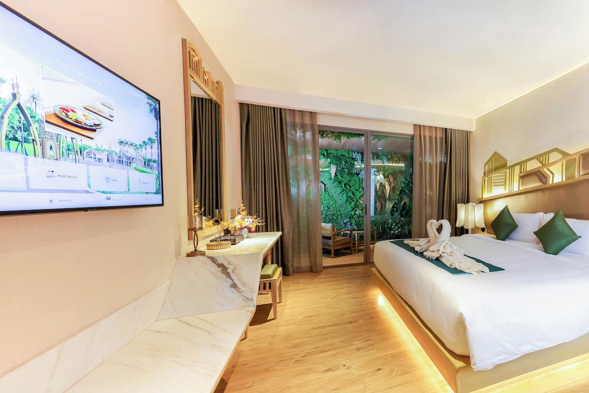 Une chambre d’hôtel avec un lit, un bureau, une télévision et une vue sur la verdure.