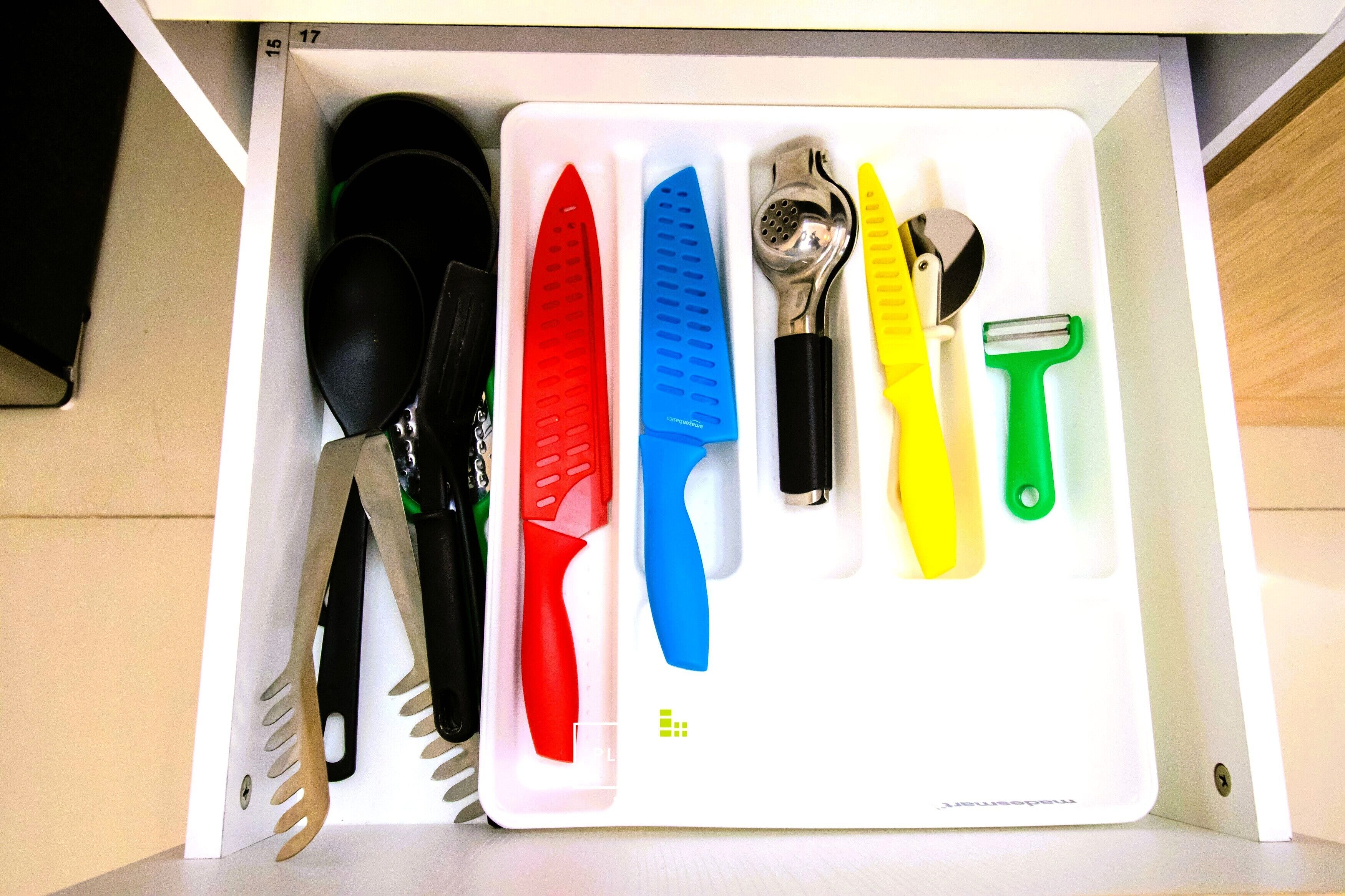 A drawer with various kitchen utensils including knives, a grater, and a peeler.