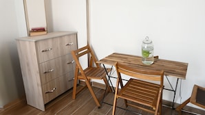 Una habitación pequeña con un escritorio de madera, dos sillas de madera, un armario y un tarro de cristal sobre el escritorio.