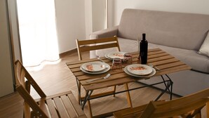 Un comedor con una mesa de madera preparada para dos personas, un sofá y una botella de vino.