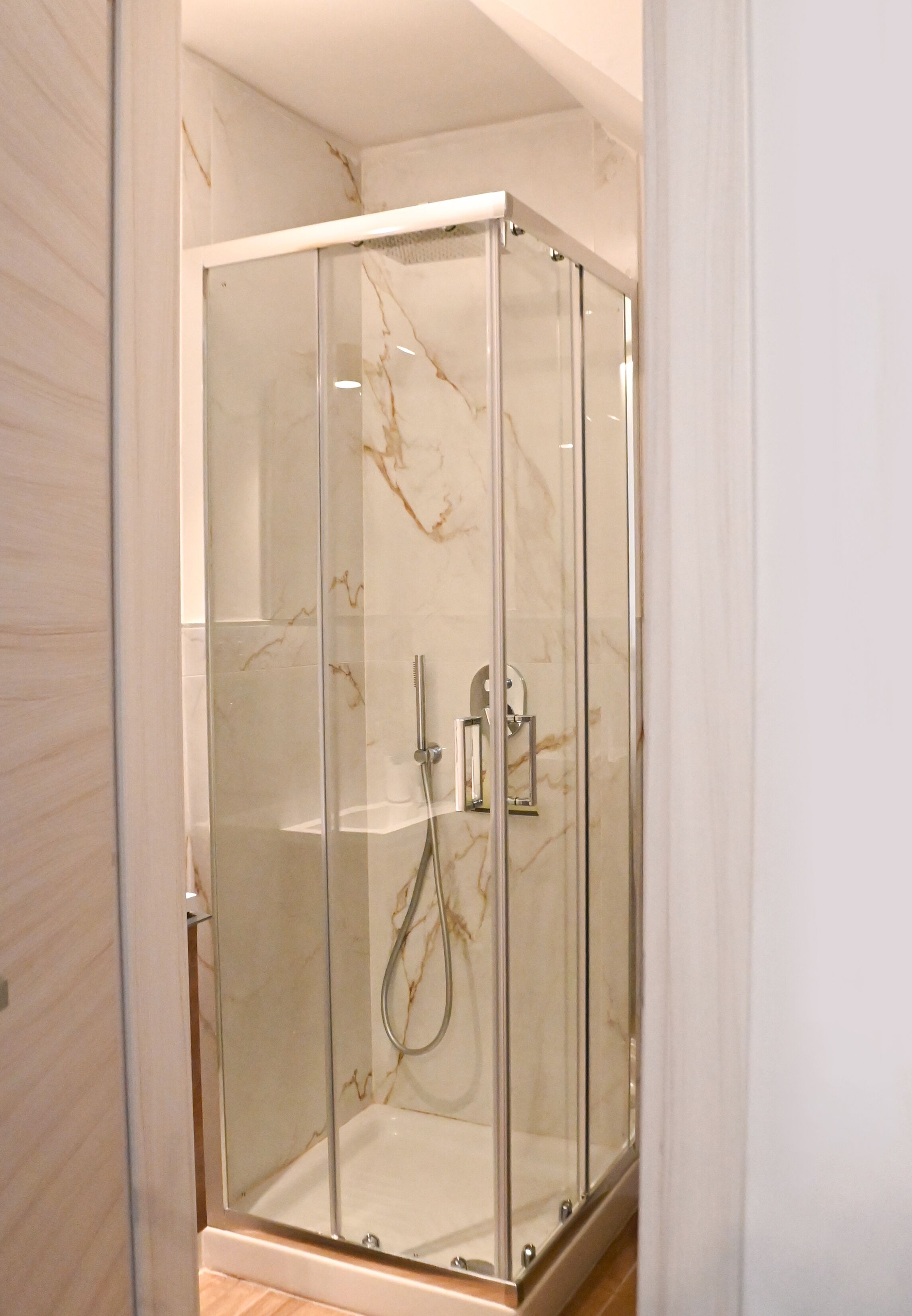 A glass-enclosed shower with a marble wall and a chrome showerhead.
