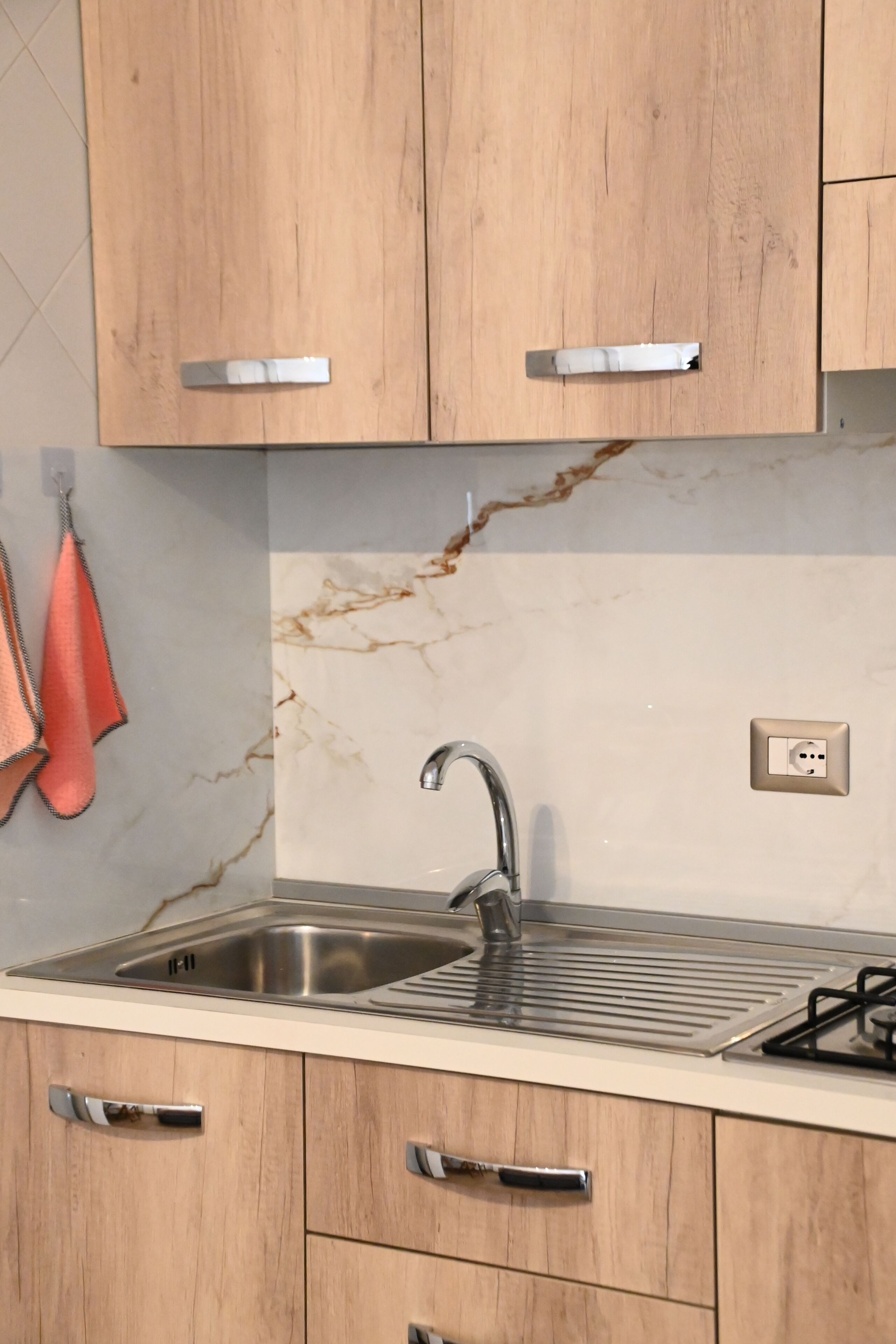 Cozinha com armários de madeira, pia de aço inoxidável e backsplash de mármore.