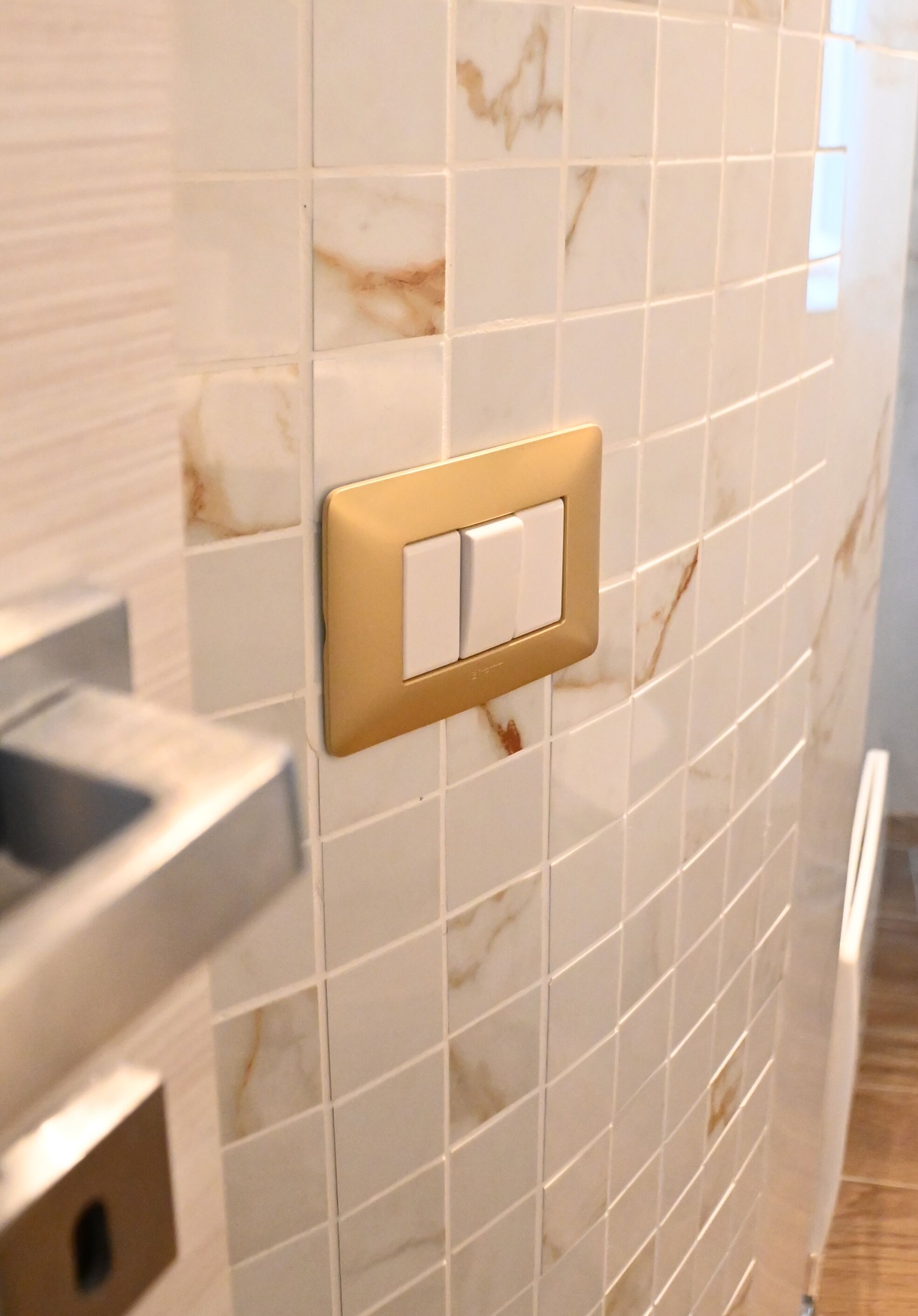 Baño con baldosas de mármol blanco y un interruptor de luz dorado.