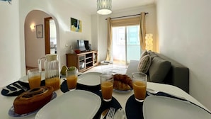 A dining area with breakfast items, a sofa, and a TV in the background. - QUARTEIRA CENTRAL BEACH 1 by HOMING (Quarteira)