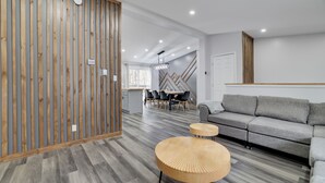 A modern living room with a grey sofa, wooden accents, and a dining area with a wooden table and chairs.